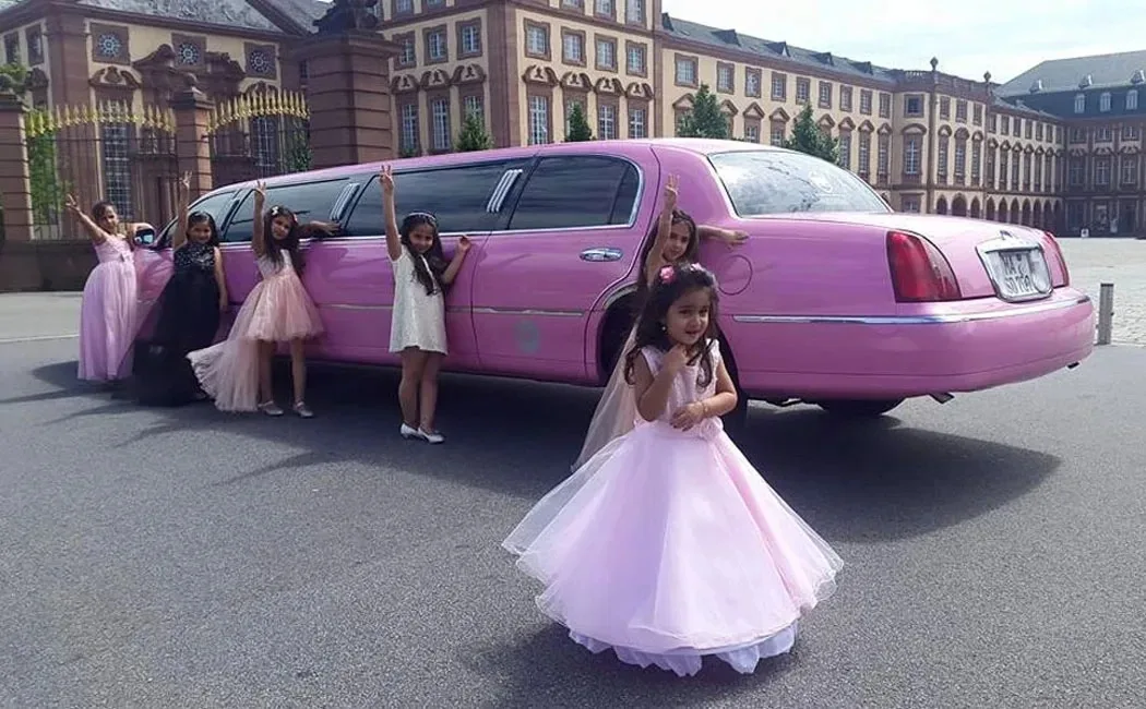 Mädchen in festlichen Kleidern posieren vor der pinken Stretchlimousine vor einem Barockschloss