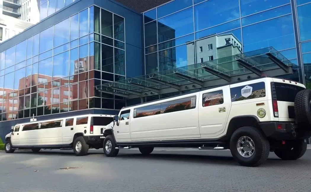 Zwei weiße Hummer-H2-Stretchlimousinen stehen hintereinander vor einem Glasgebäude