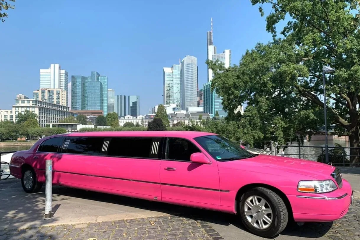 Pinke Lincoln-Stretchlimousine am Flussufer vor einer Hochhaus-Skyline
