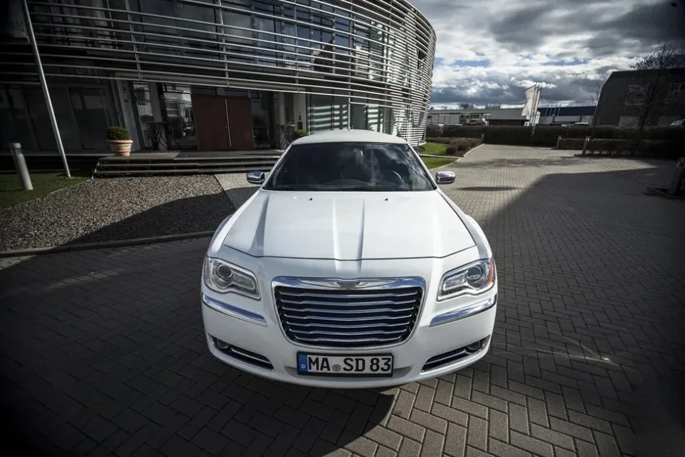 Weißer Chrysler 300C in Frontansicht vor einem modernen Gebäude