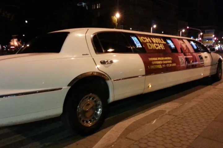 Weiße Limousine mit Werbebeklebung bei Nacht