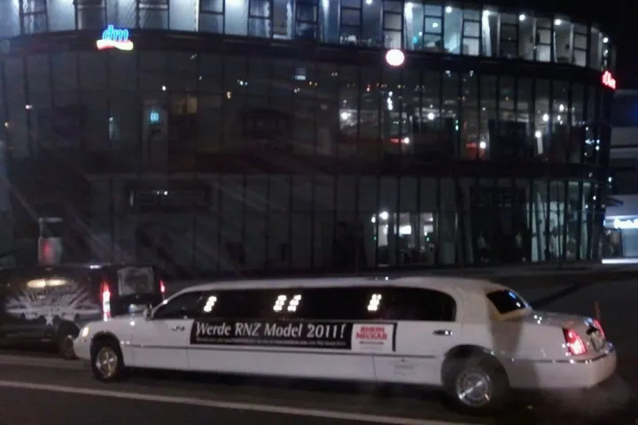 Weiße Limousine mit Werbefolie vor einem beleuchteten Gebäude