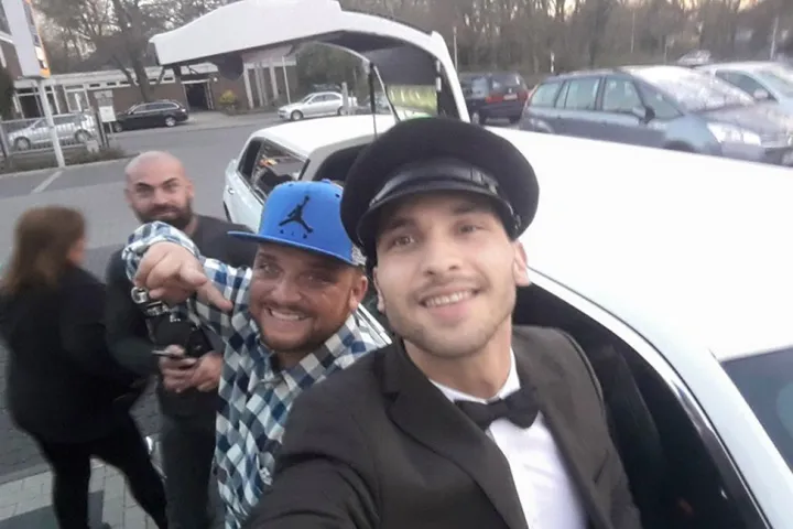 Gäste und ein Chauffeur mit Schirmmütze an einer Limousine