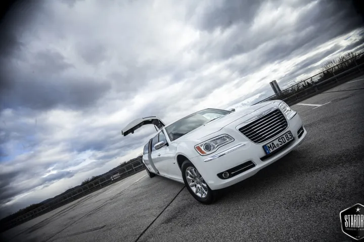 Weißer Chrysler 300C mit geöffneter Flügeltür vor dramatischem Wolkenhimmel