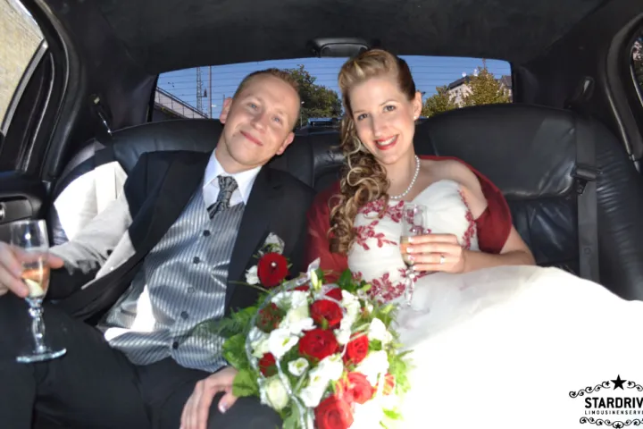 Brautpaar mit Sektglas und Brautstrauß im Innenraum der Limousine