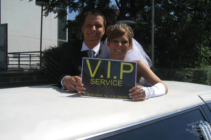 Brautpaar mit VIP-Service-Schild auf der weißen Limousine