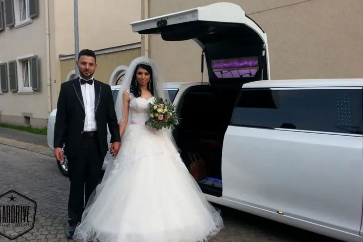 Brautpaar vor der weißen Limousine mit geöffnetem Kofferraum