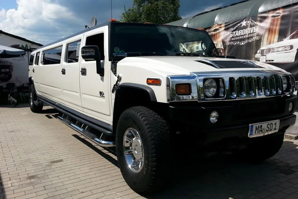 Weißer Hummer H2 von vorn rechts vor einer STARDRIVE-Werbeplane
