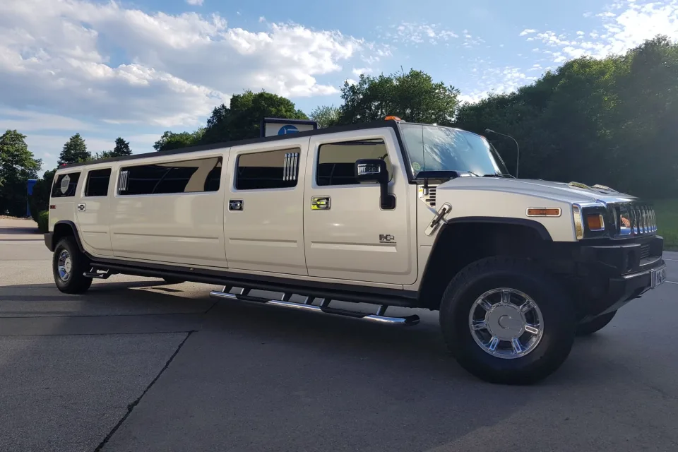 Weißer Hummer H2 Stretch-Limousine von der Seite im Abendlicht vor Bäumen und blauem Himmel