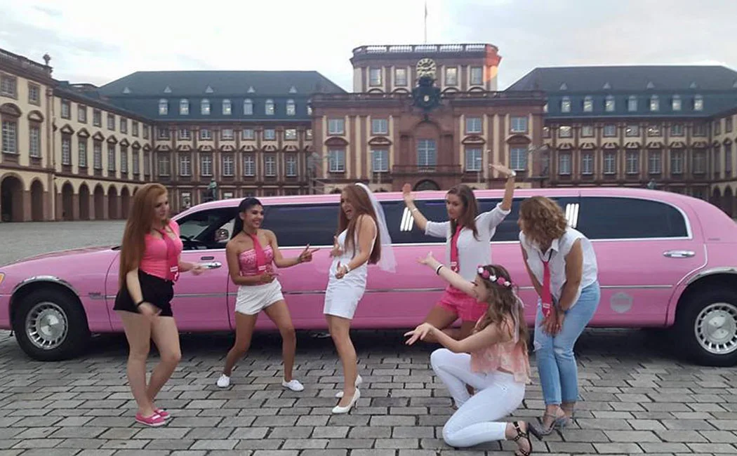Gruppe von Frauen feiert einen Junggesellinnenabschied vor der pinken Stretchlimousine vor dem Mannheimer Schloss